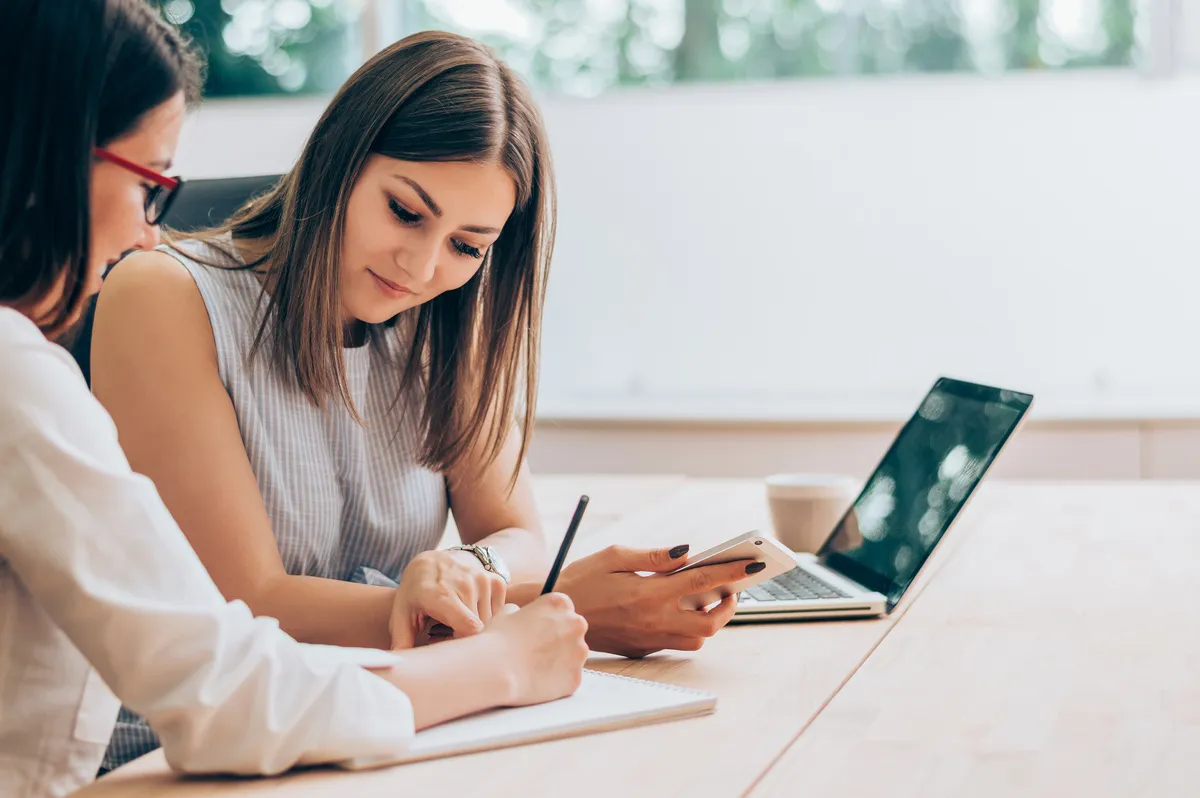 Dos mujeres estudiando juntas en una mesa con portátil y libreta