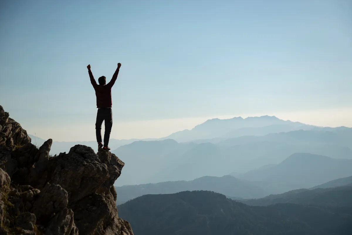 Person mit erhobenen Armen auf einem Berggipfel